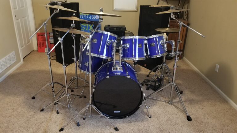 A blue drum set up in a carpeted basement two large speakers behind it.